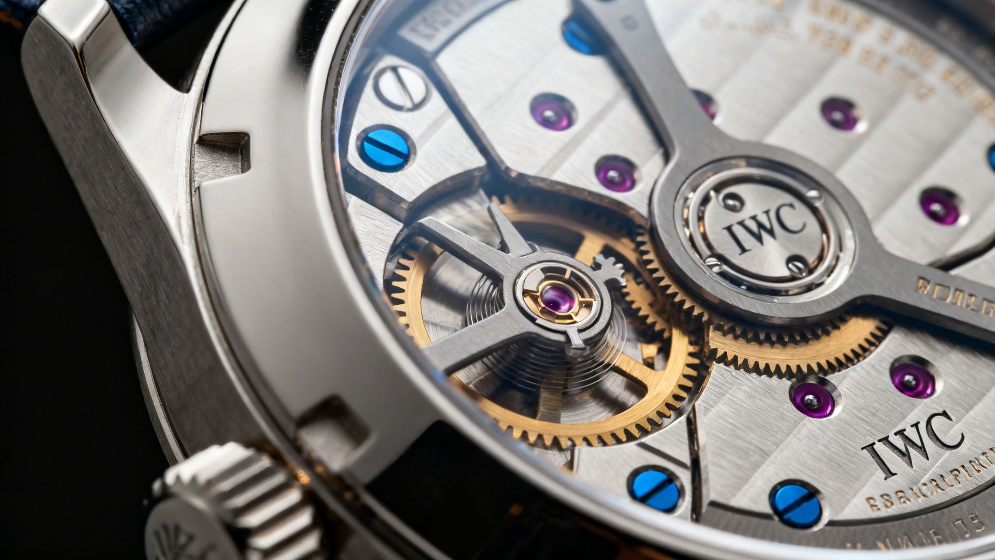 Close-up of an IWC watch movement, showing intricate golden gears, purple jewels, and blue screws.