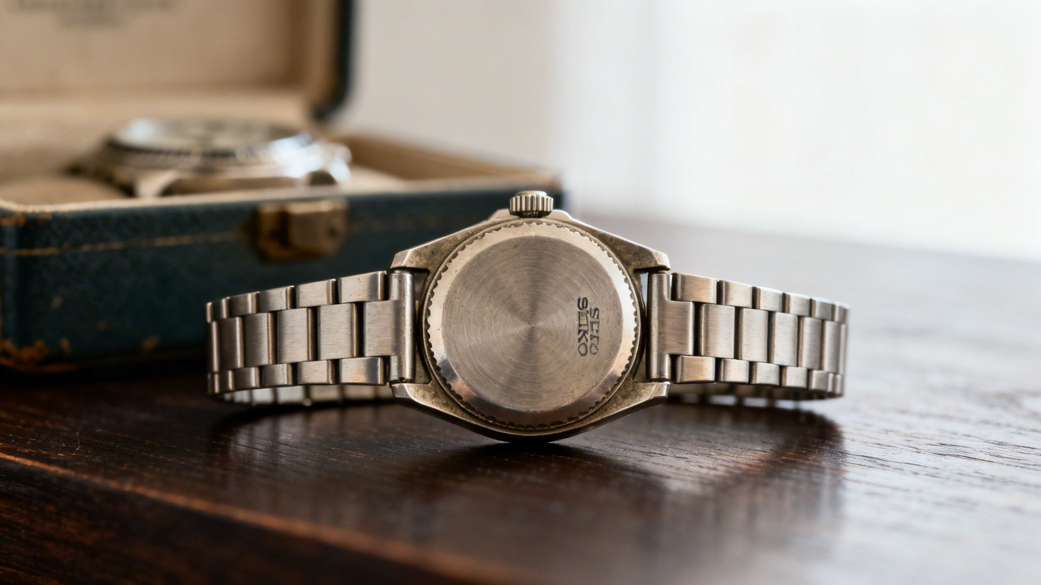 Back of a silver Seiko watch with a metal jubilee bracelet on a wooden table.