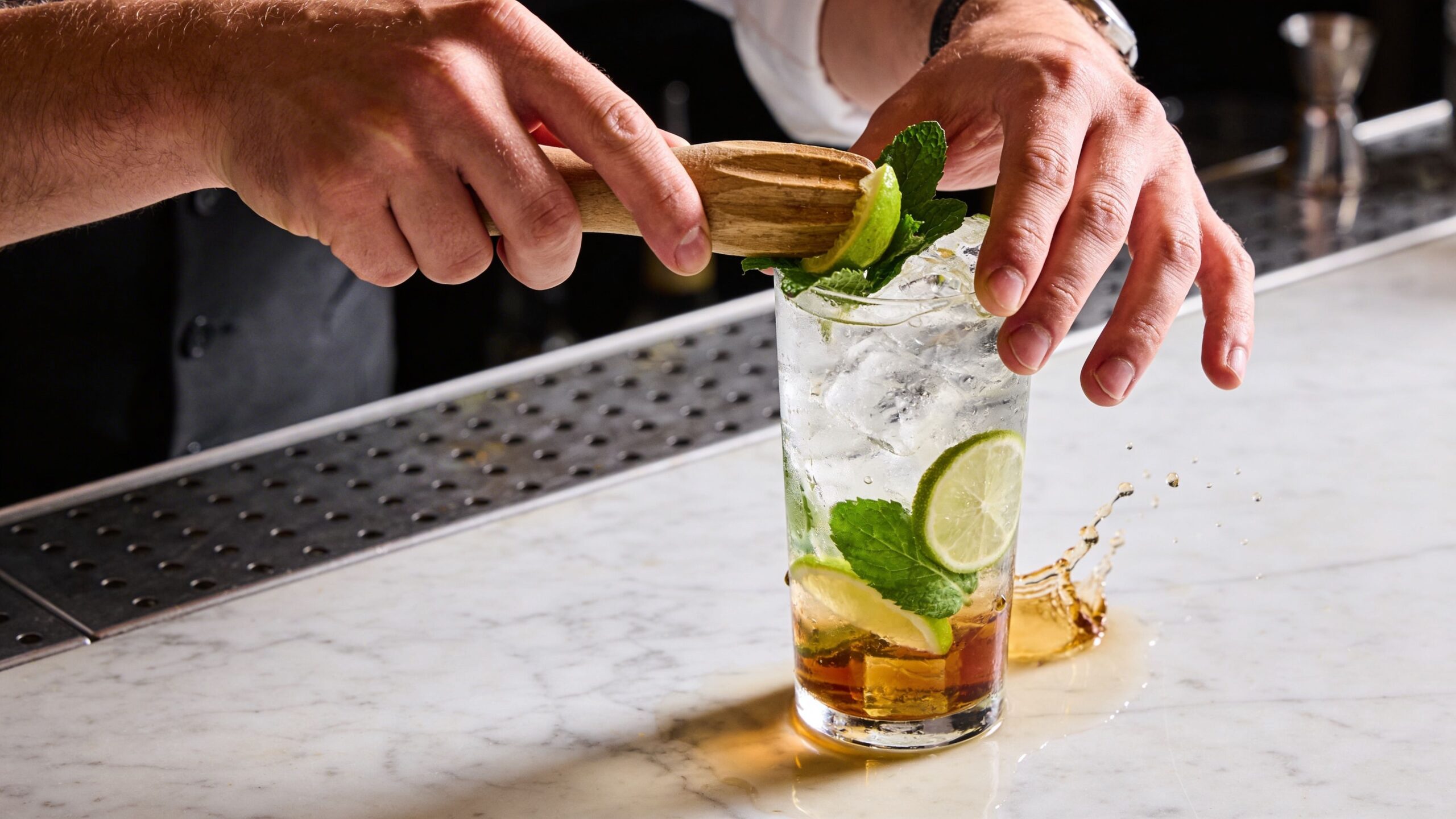 A professional bartender prepares a refreshing cocktail, muddling fresh lime and mint into a glass with ice.