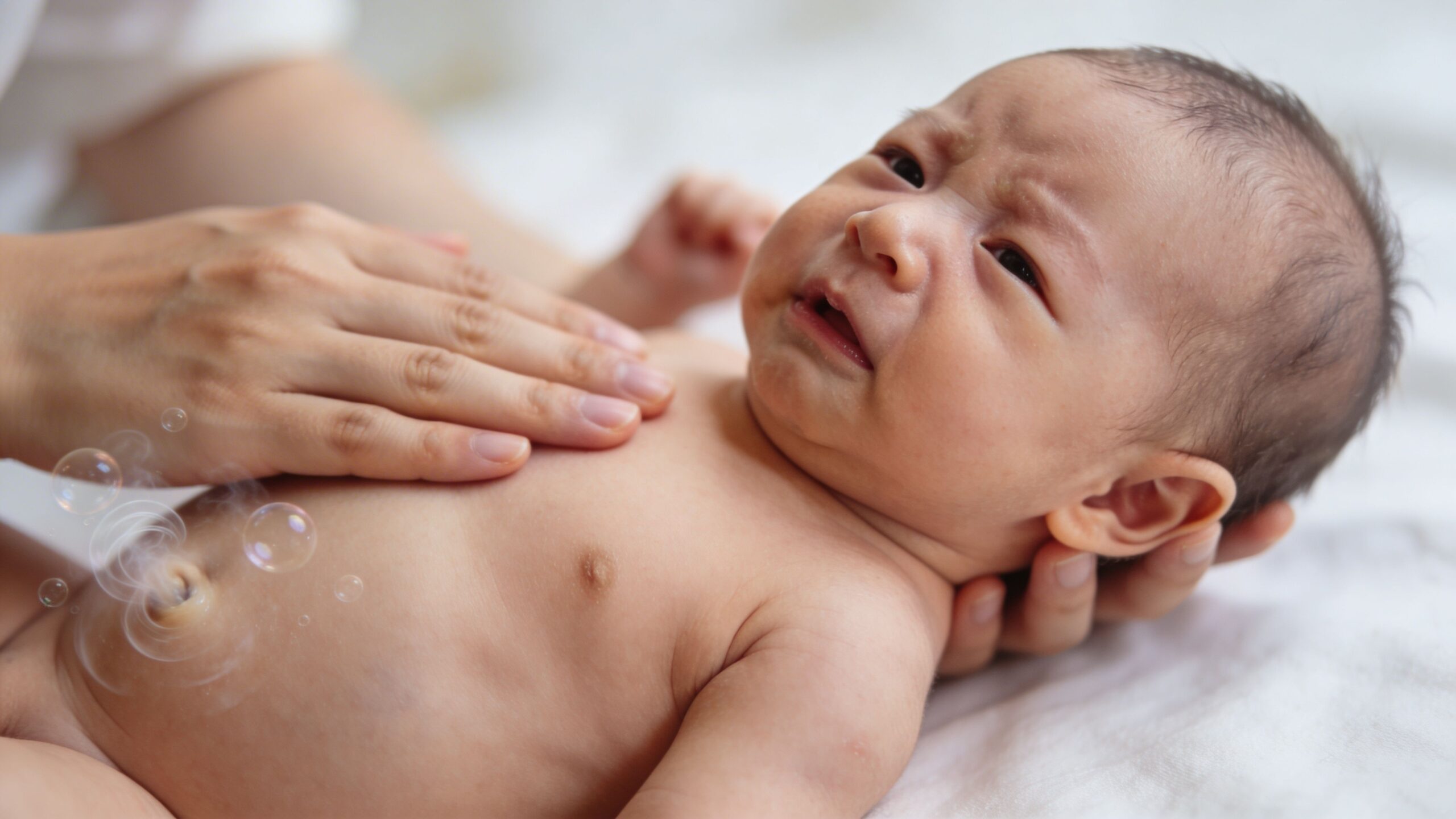 A caring parent gently burping their crying newborn baby while lying down on a soft white bed